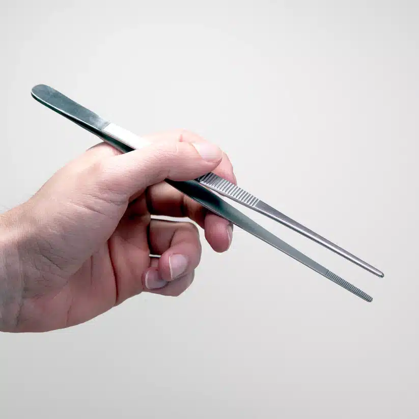 A hand holds metal tweezers against a light background, showcasing the precision needed when using the Plant Cell Tissue Culture Starter Kit.