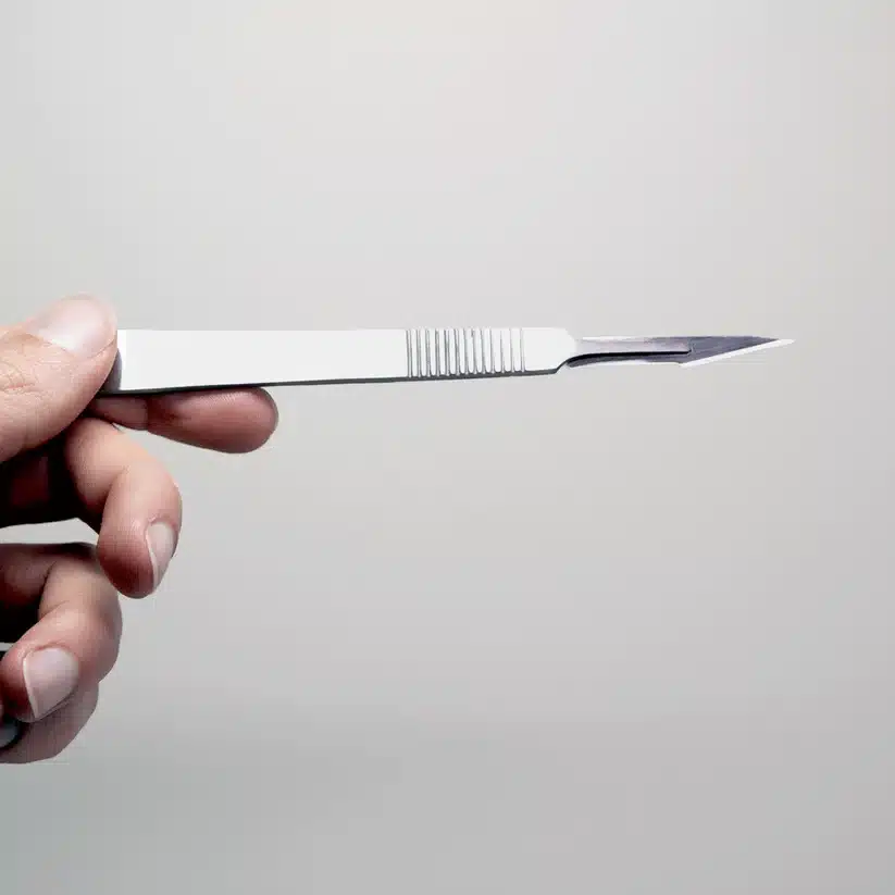 A hand holds a surgical scalpel, ready to use with the Plant Cell Tissue Culture Starter Kit, against a plain light background.