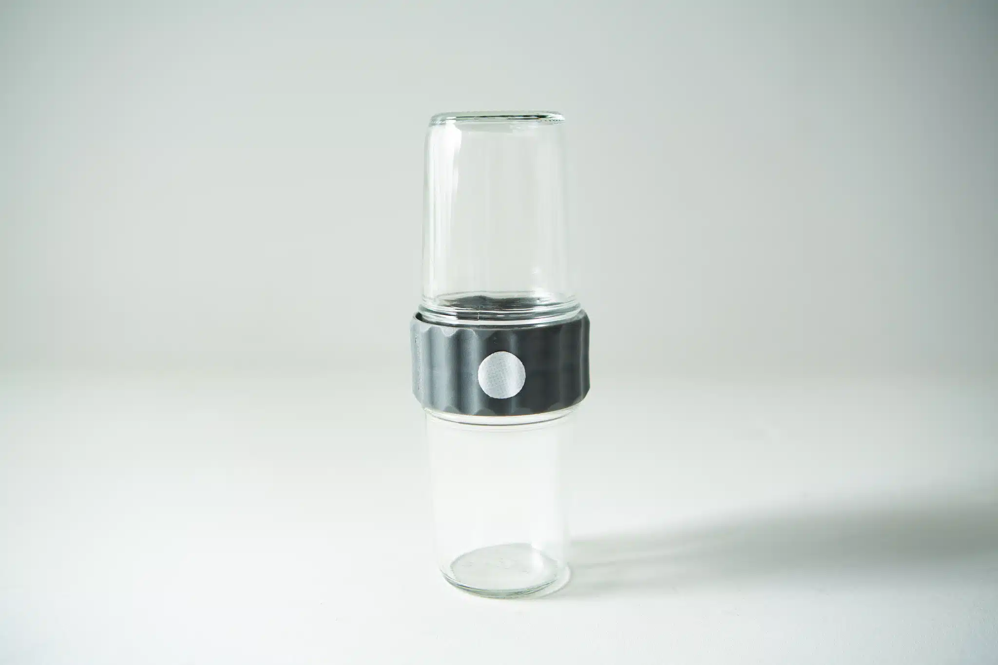 Two clear glass cups stacked with a metallic, ribbed Plant Cell Biocouplerâ„¢ Neck band around the middle, set against a plain white background.