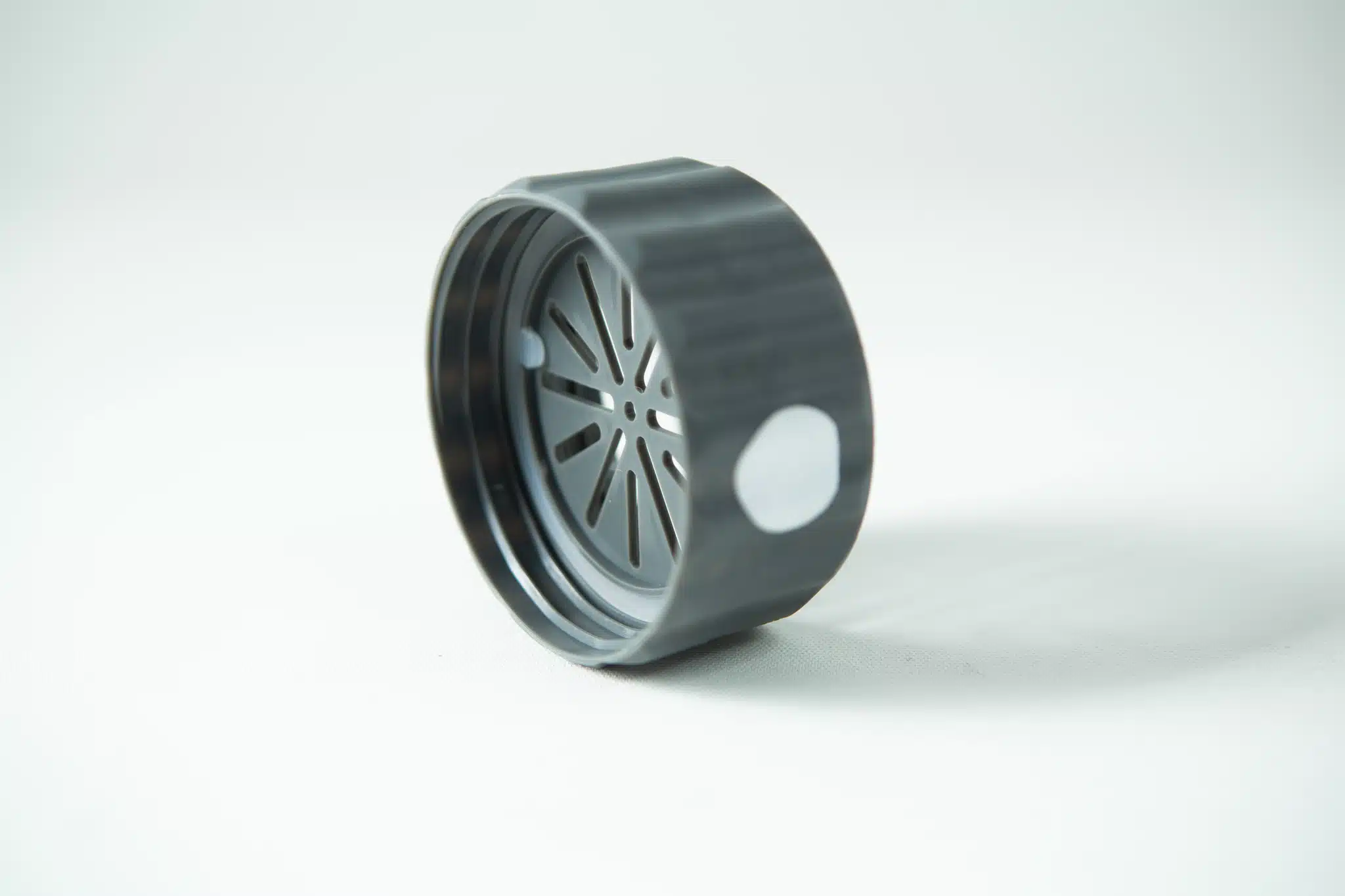 Black plastic lid with a circular slotted design, designed as a cover for the Plant Cell Biocouplerâ„¢ Neck, shown on a white surface under soft lighting.