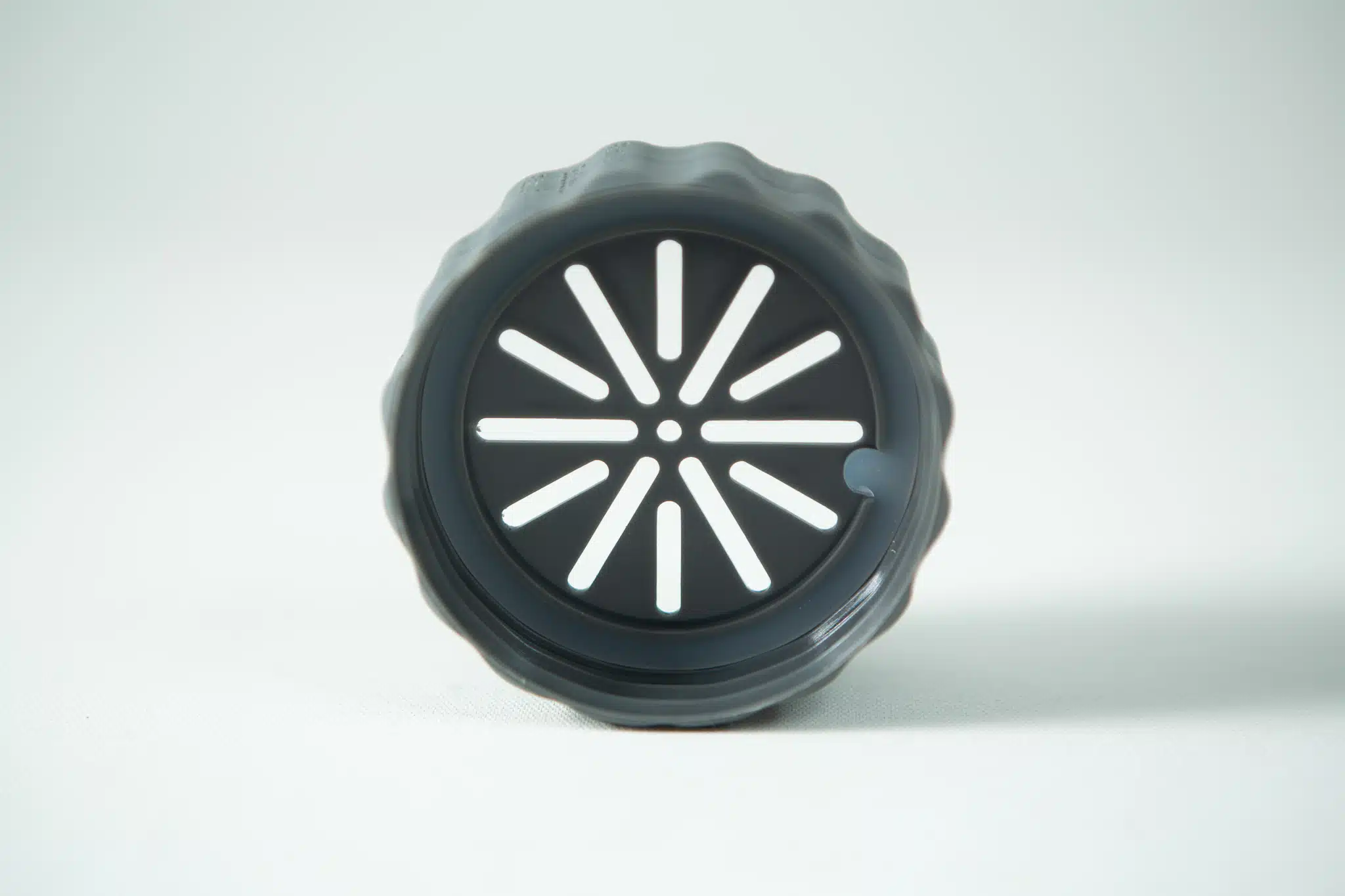 A black circular object with radial slits in a sunburst pattern, resembling the Plant Cell Biocouplerâ„¢ Neck, viewed from the front.