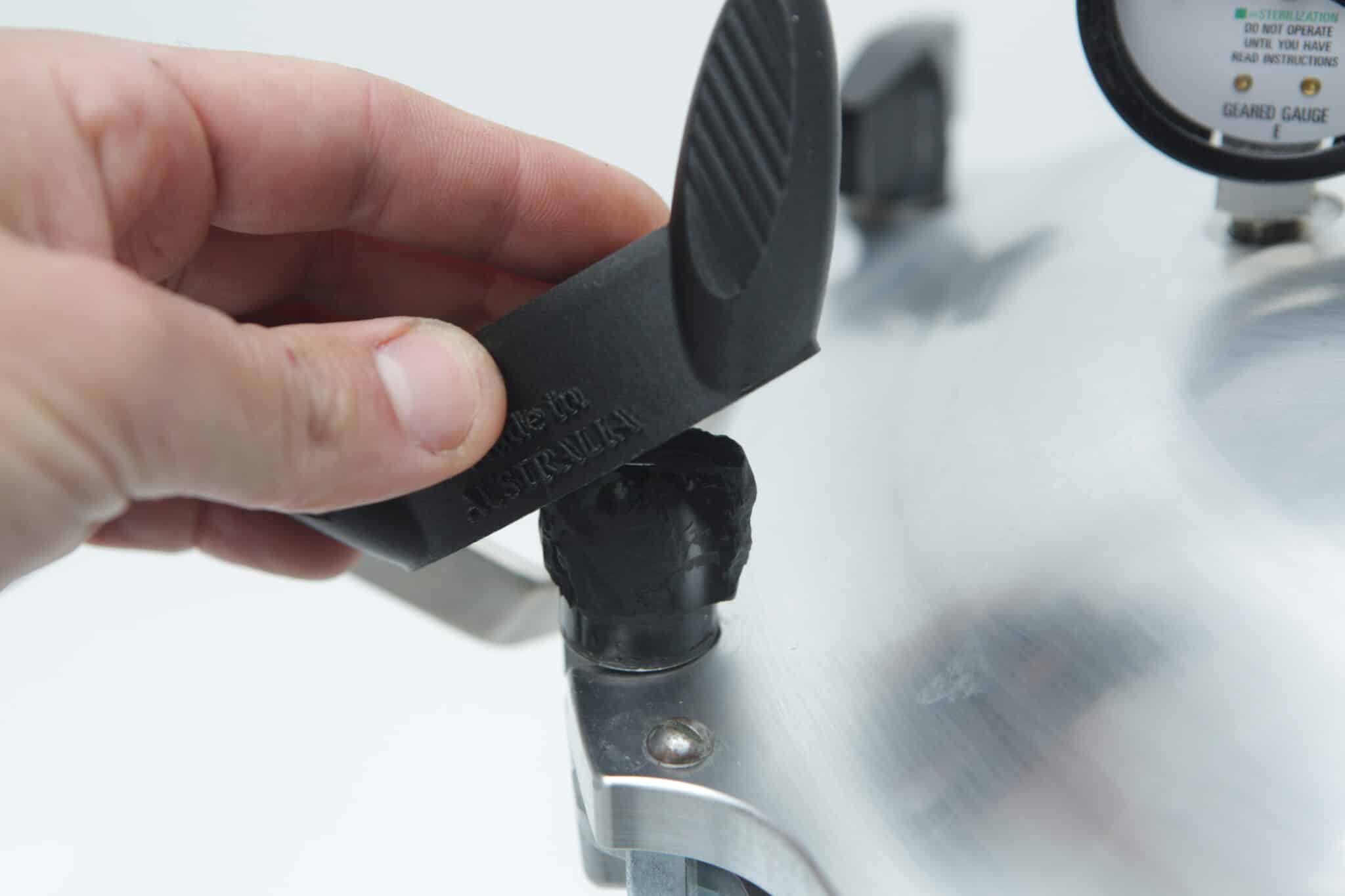 A hand uses the Rootlab Original 3D Printed Wingnut Wrench to remove a black rubber plug from an All American Steriliser pressure cooker lid.