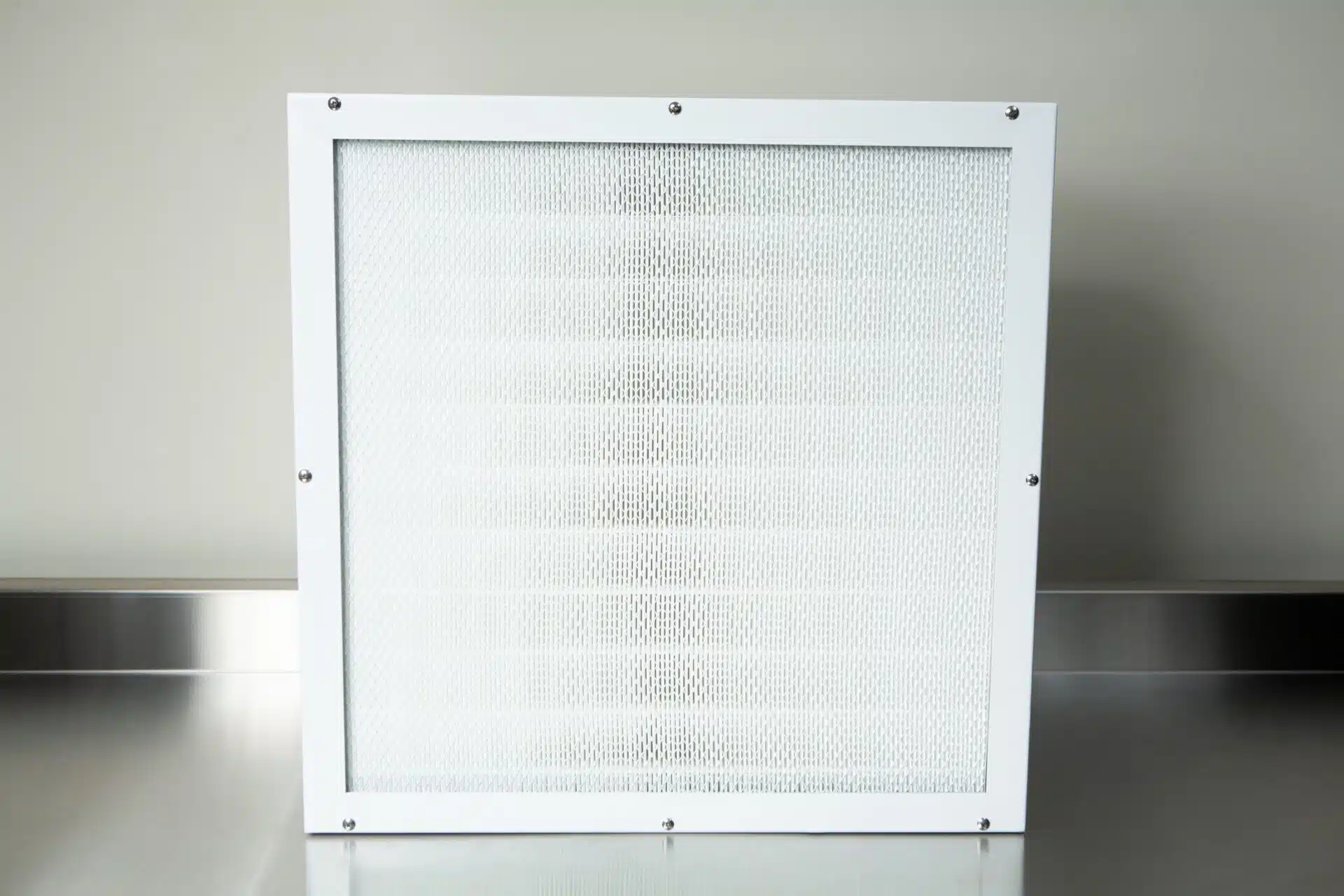 The Laminar Flow Hood HEPA Airfilter H14 w/prefilter 60x60x35cm, featuring a white frame and mesh screen, sits on a metal surface against a neutral wall—ideal for use in laminar flow hoods.