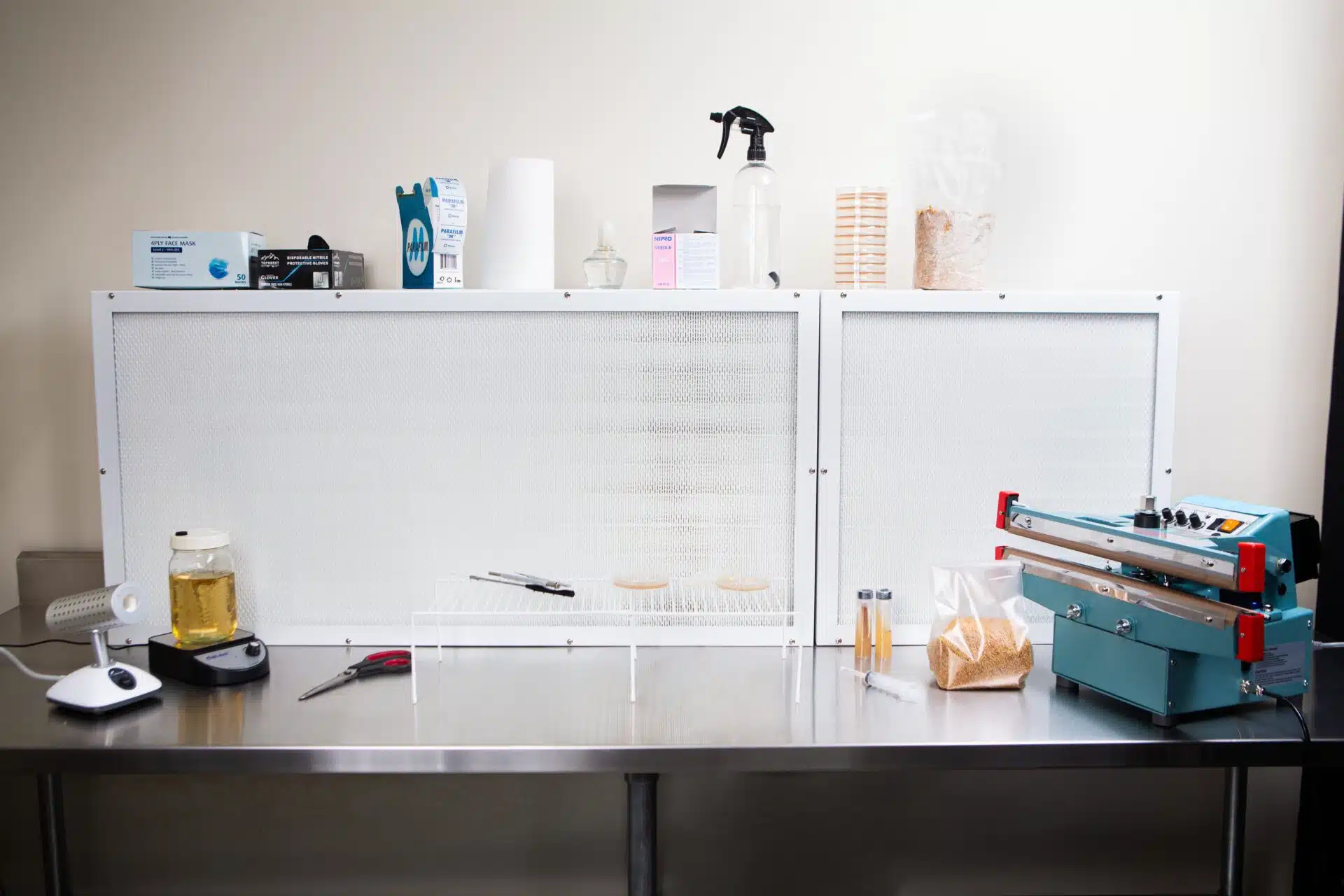 A laboratory workbench with sterilization equipment, tools, petri dishes, a heat sealer, and a Laminar Flow Hood HEPA Airfilter H14 w/prefilter 60x60x35cm.
