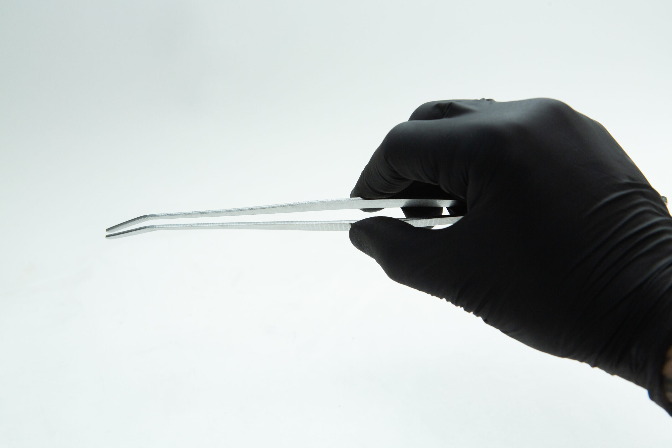 A hand in a black glove holds metal tweezers against a plain white background.
