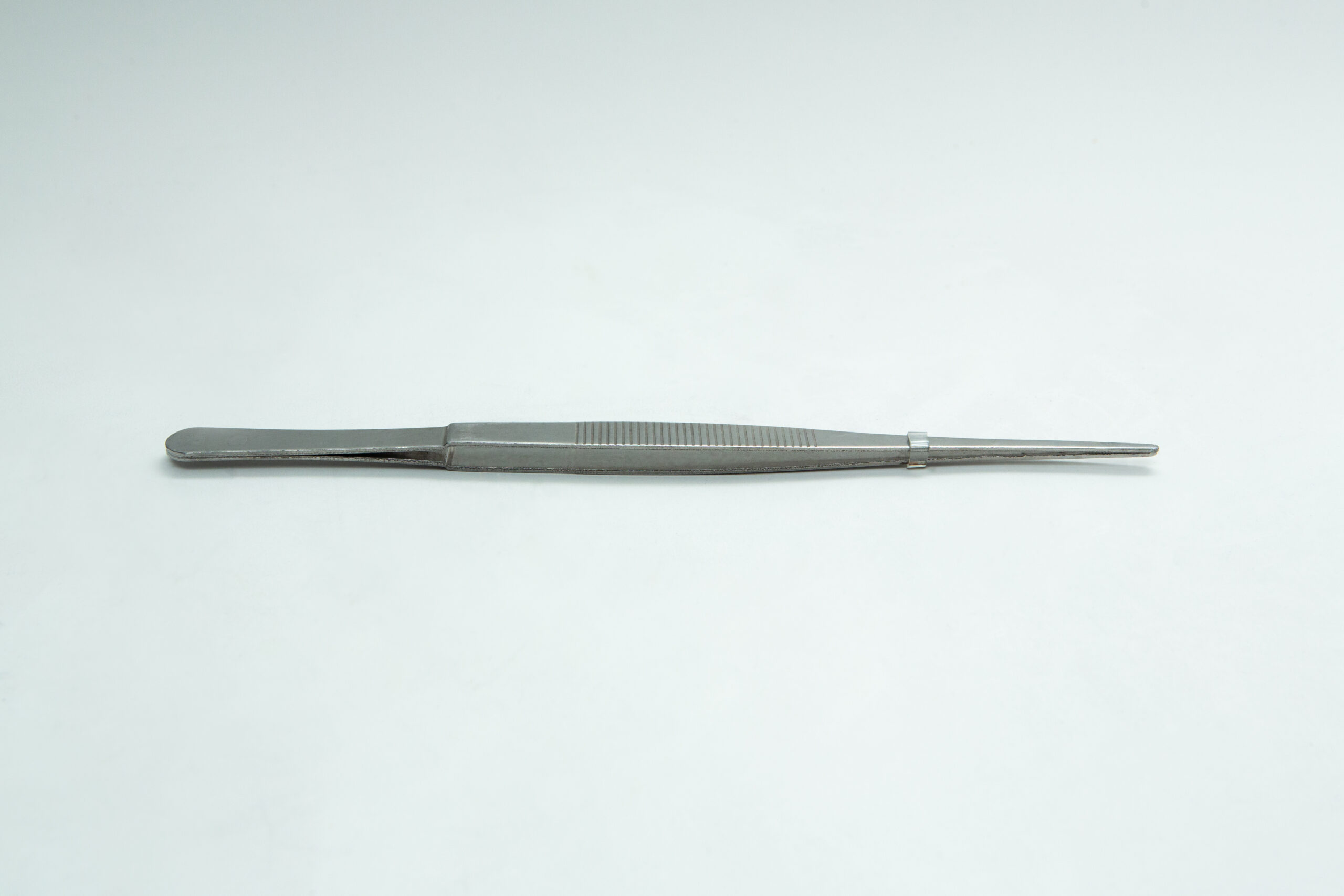 A stainless steel tweezer with a textured grip lies on a plain white surface.
