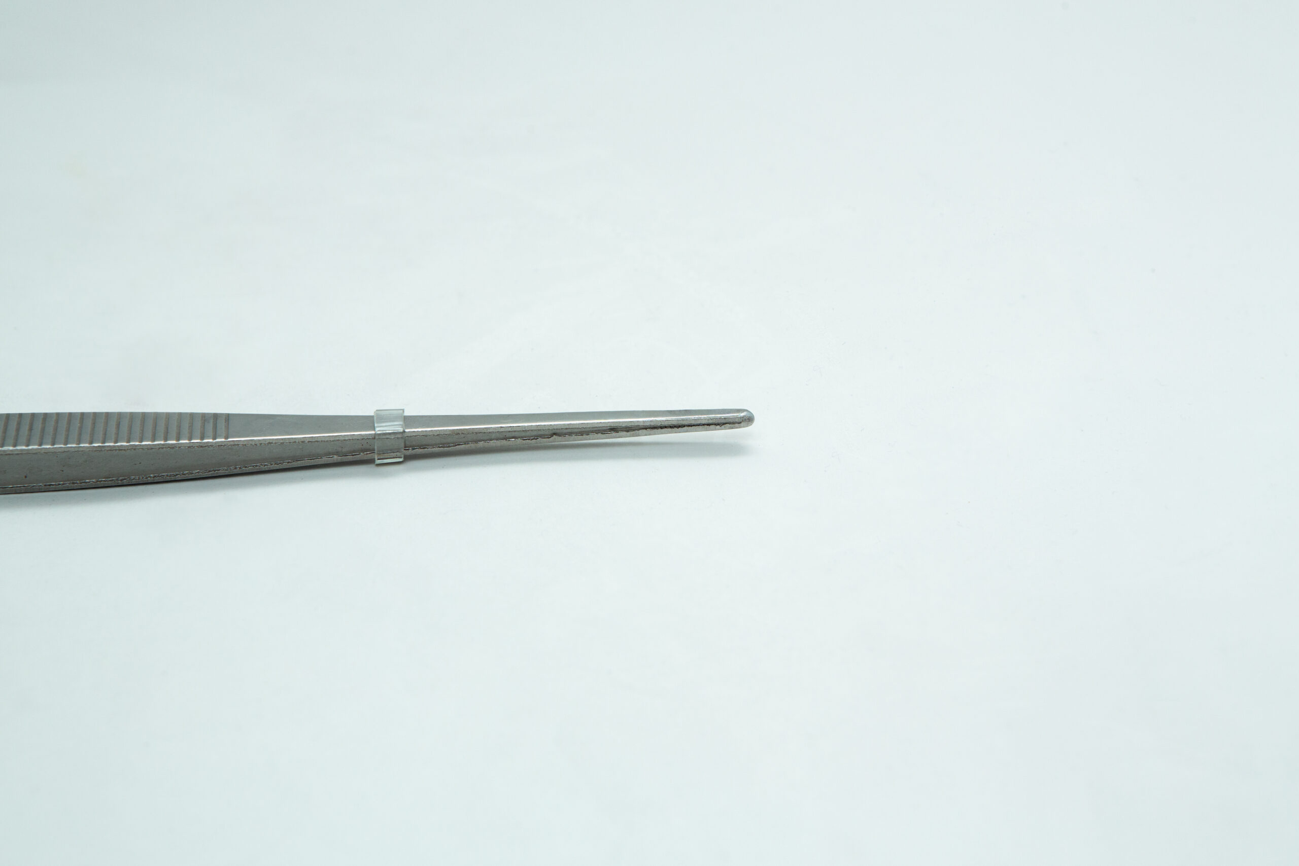 A pair of metal tweezers lies on a plain white surface, positioned towards the left side of the image.