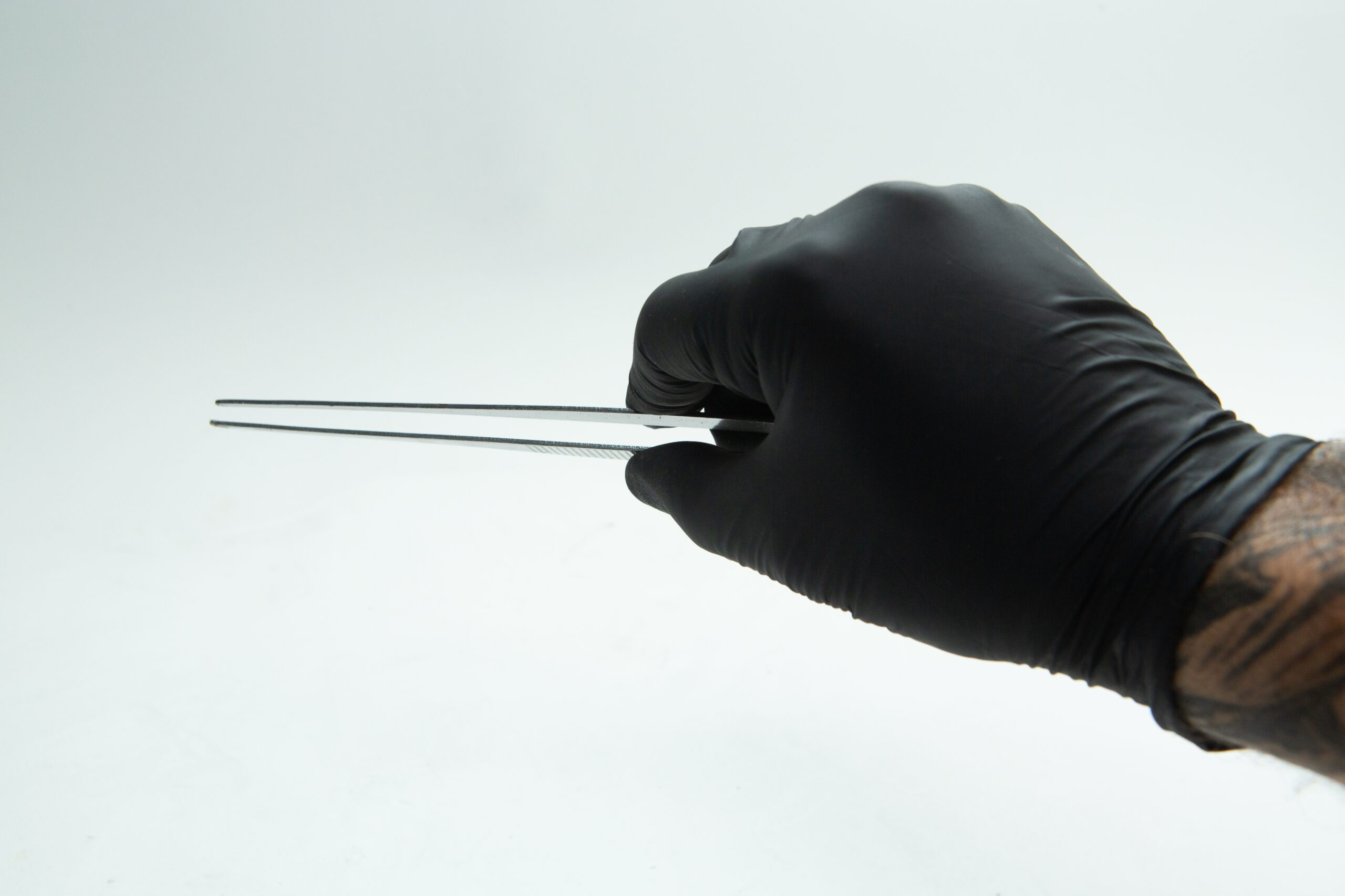 Gloved hand holding metal tweezers against a plain white background.