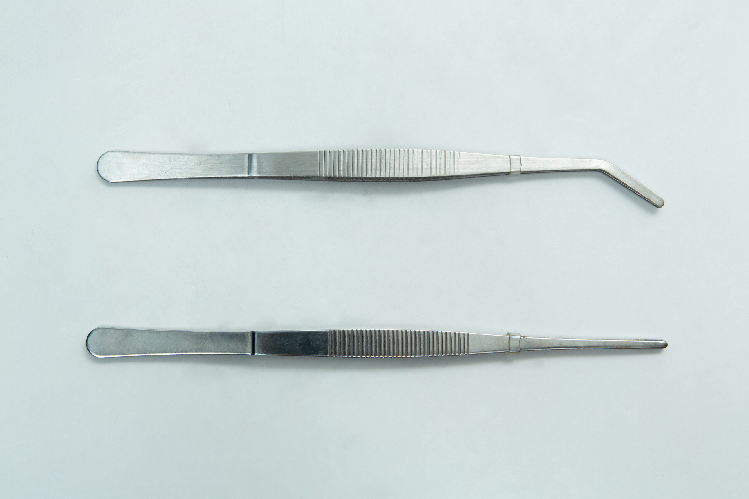 Two stainless steel dental tweezers, one with a straight tip and one with an angled tip, on a white background.