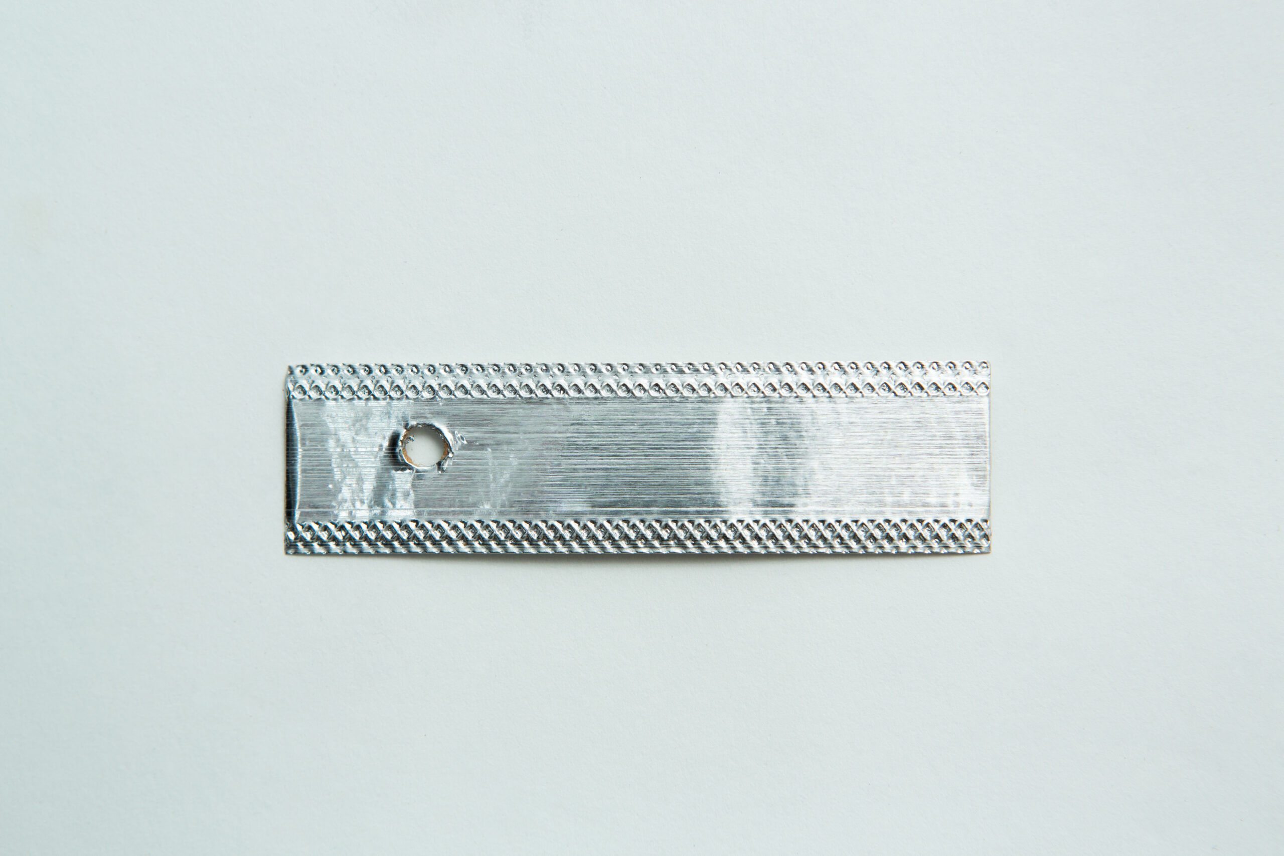 A rectangular silver metal piece with a hole on one end, displayed on a plain white background.