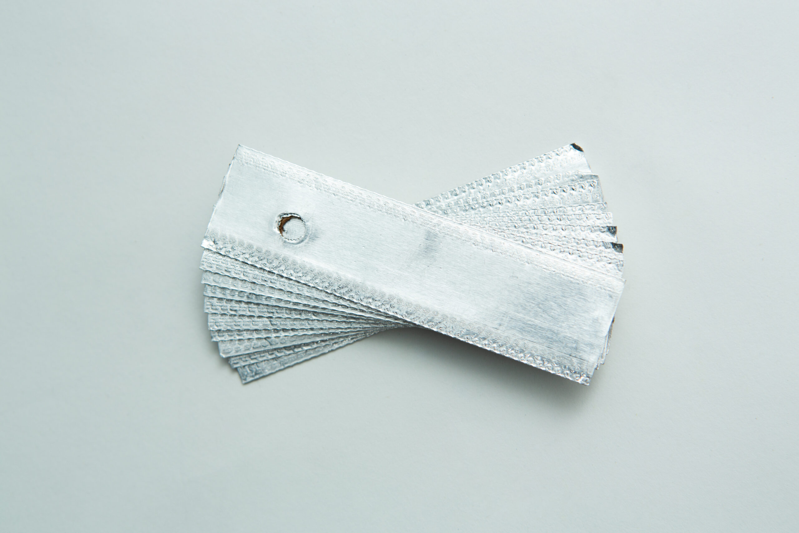A stack of small silver metallic samples, fanned out and held together by a metal ring on a white surface.