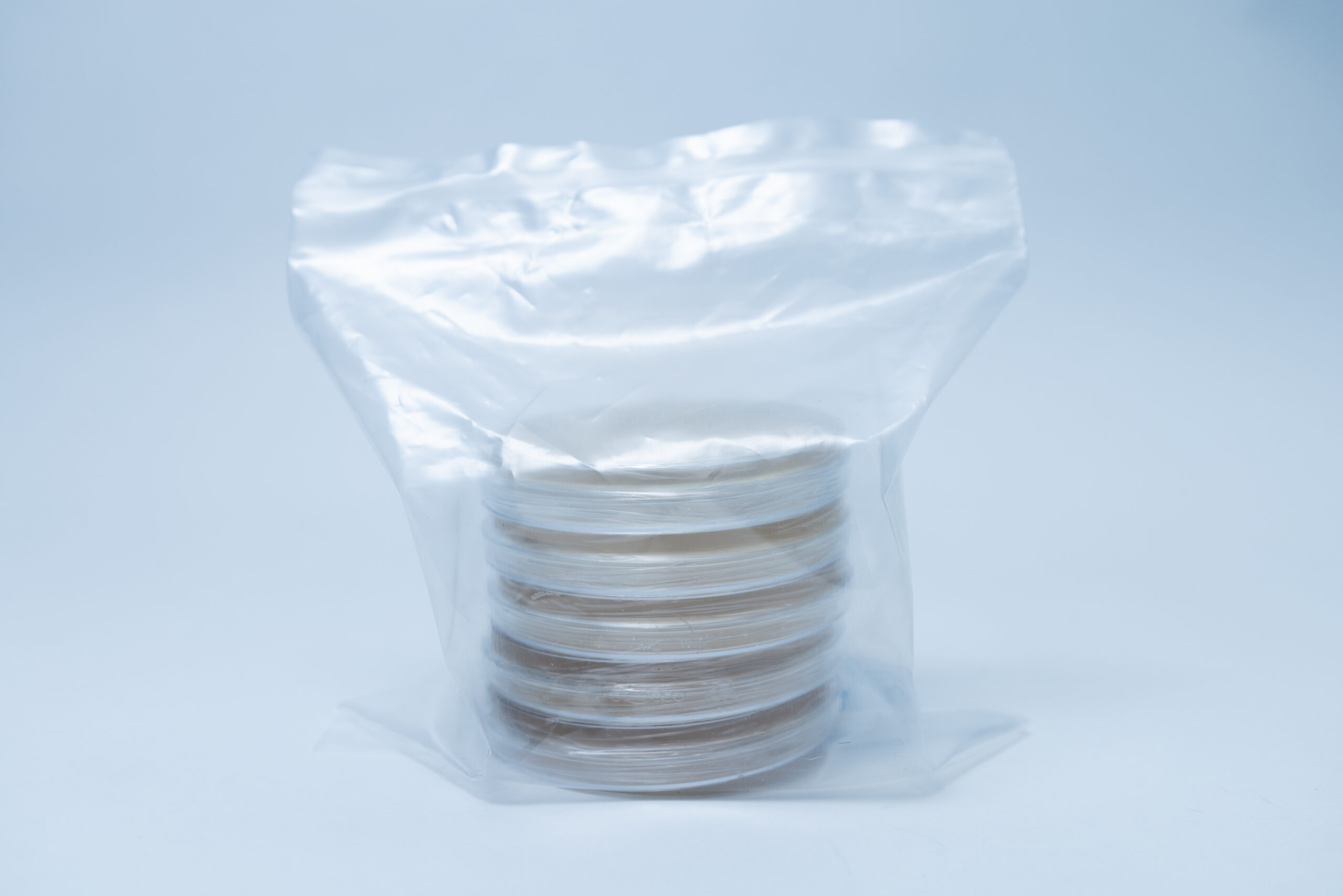 Six clear petri dishes stacked inside a transparent plastic bag on a light blue background.
