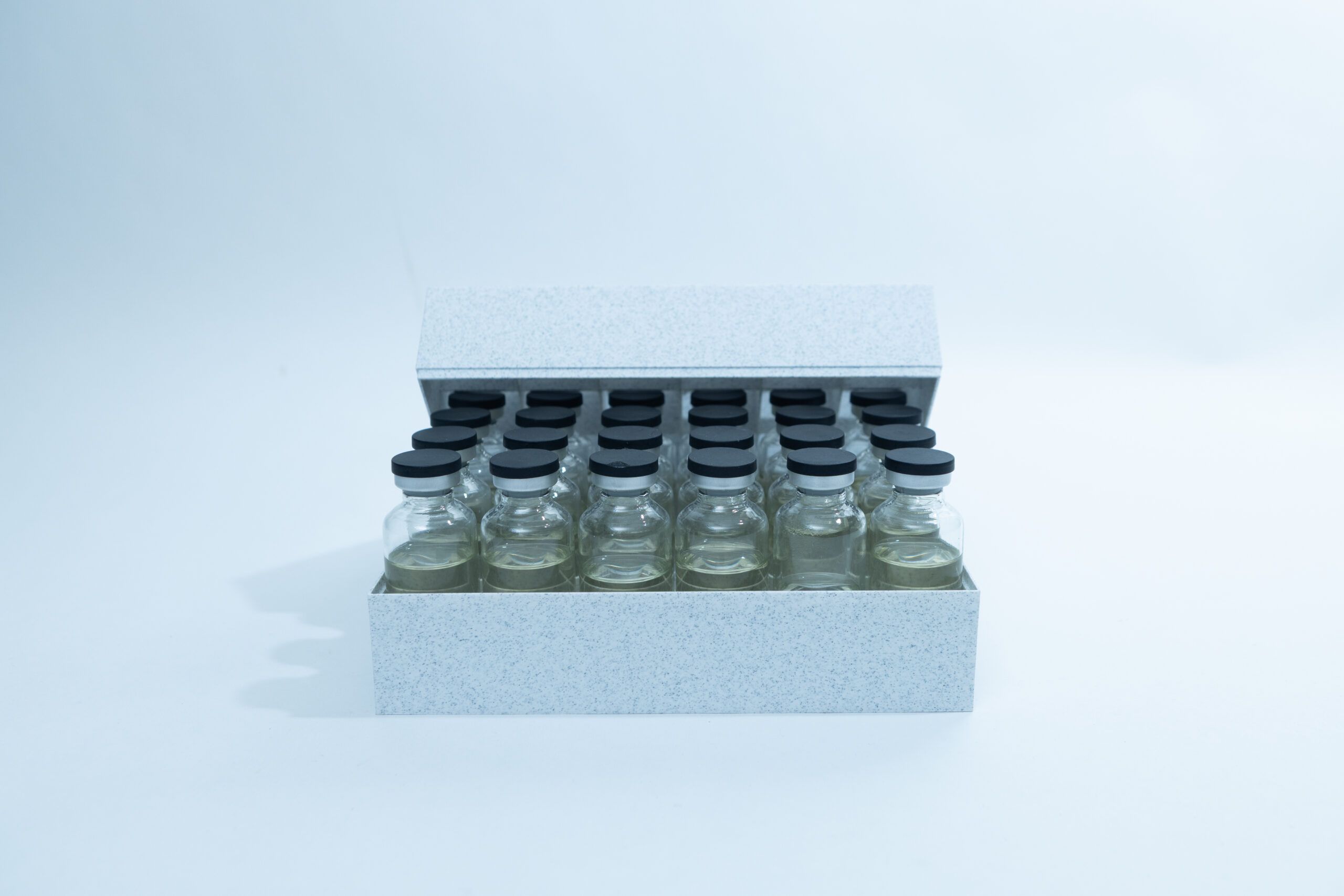A box containing multiple glass vials with black caps, arranged in neat rows on a white surface.
