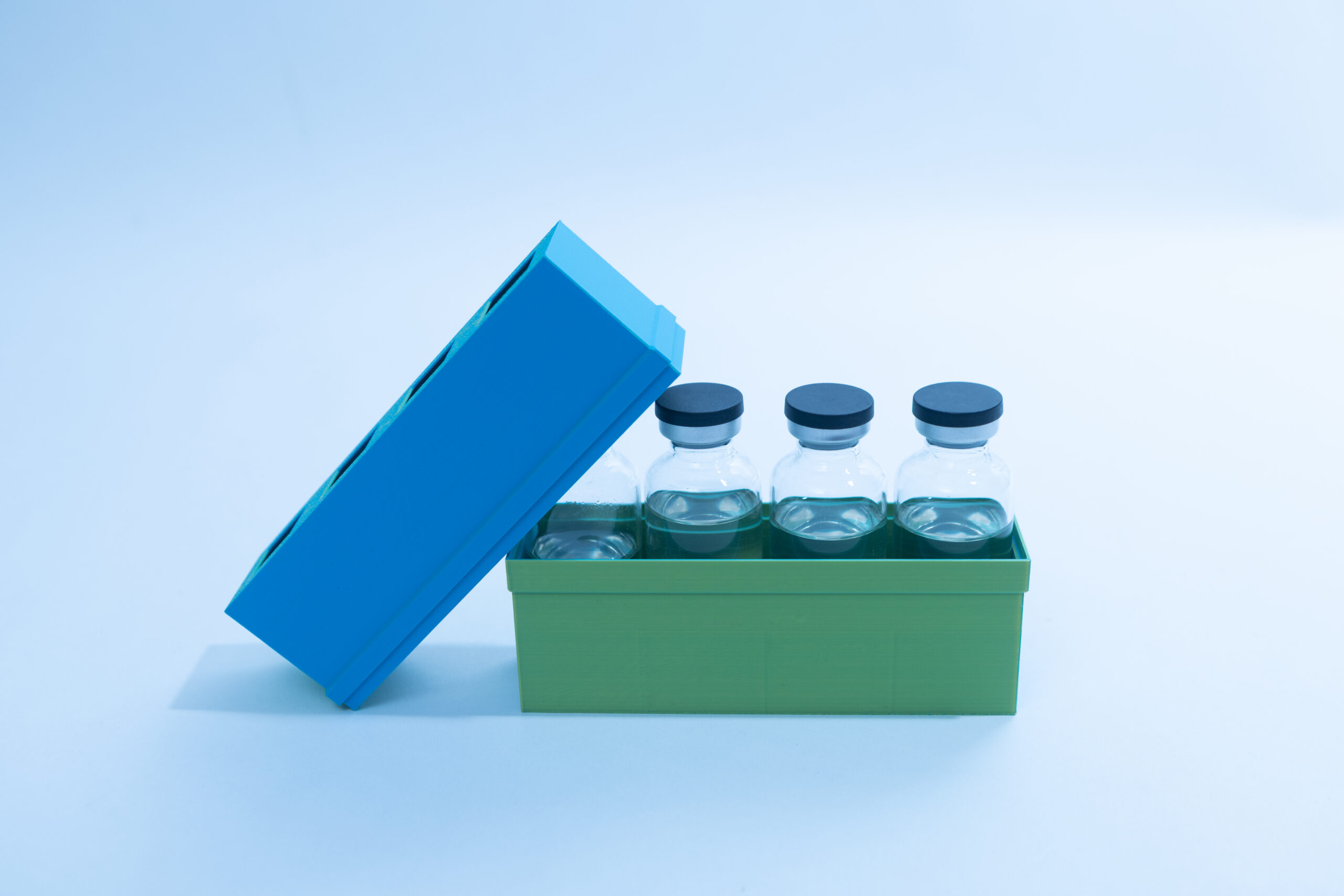 Four glass vials with black caps in a green box, blue lid partially open, on a white background.