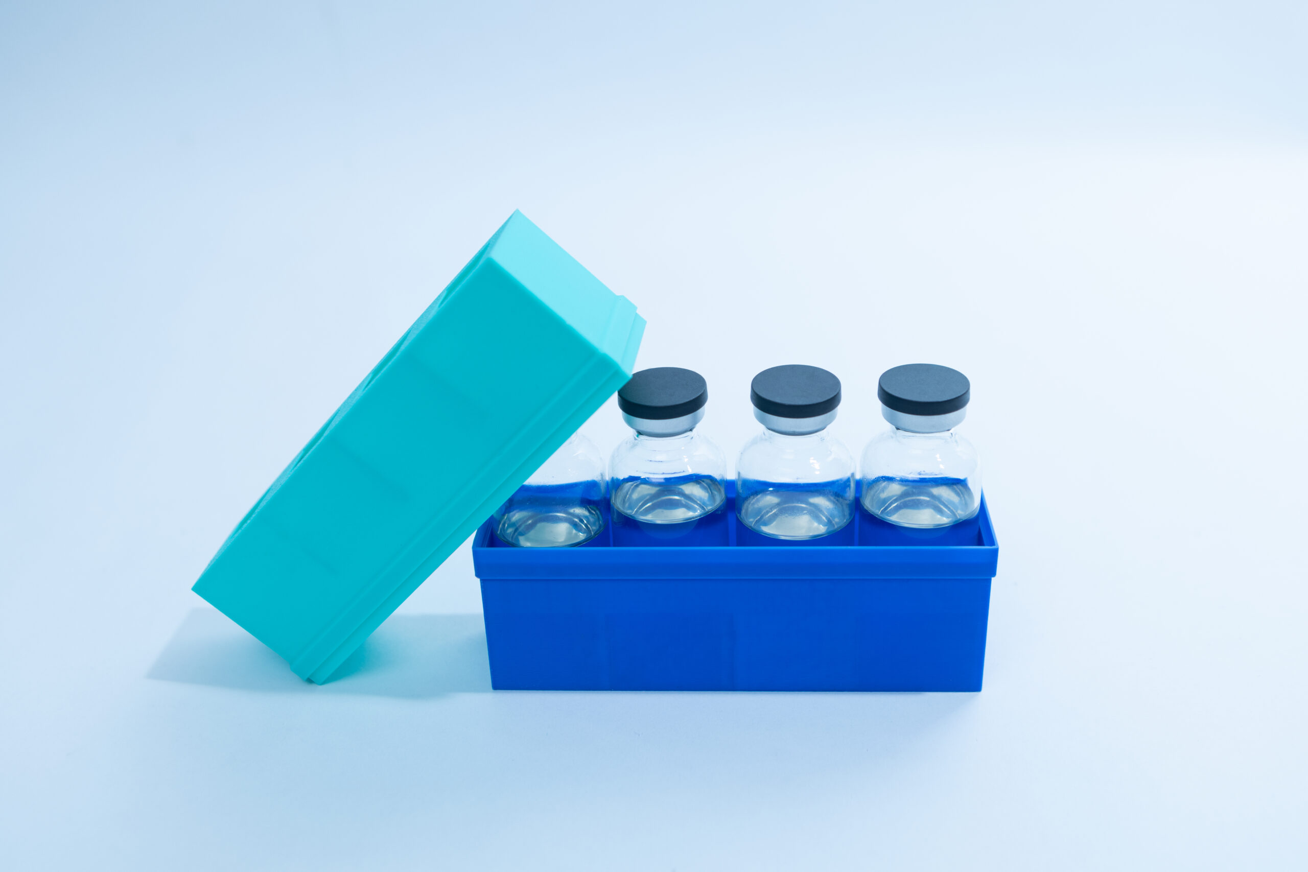 Three glass vials with black caps in a blue container with a teal lid, on a light background.