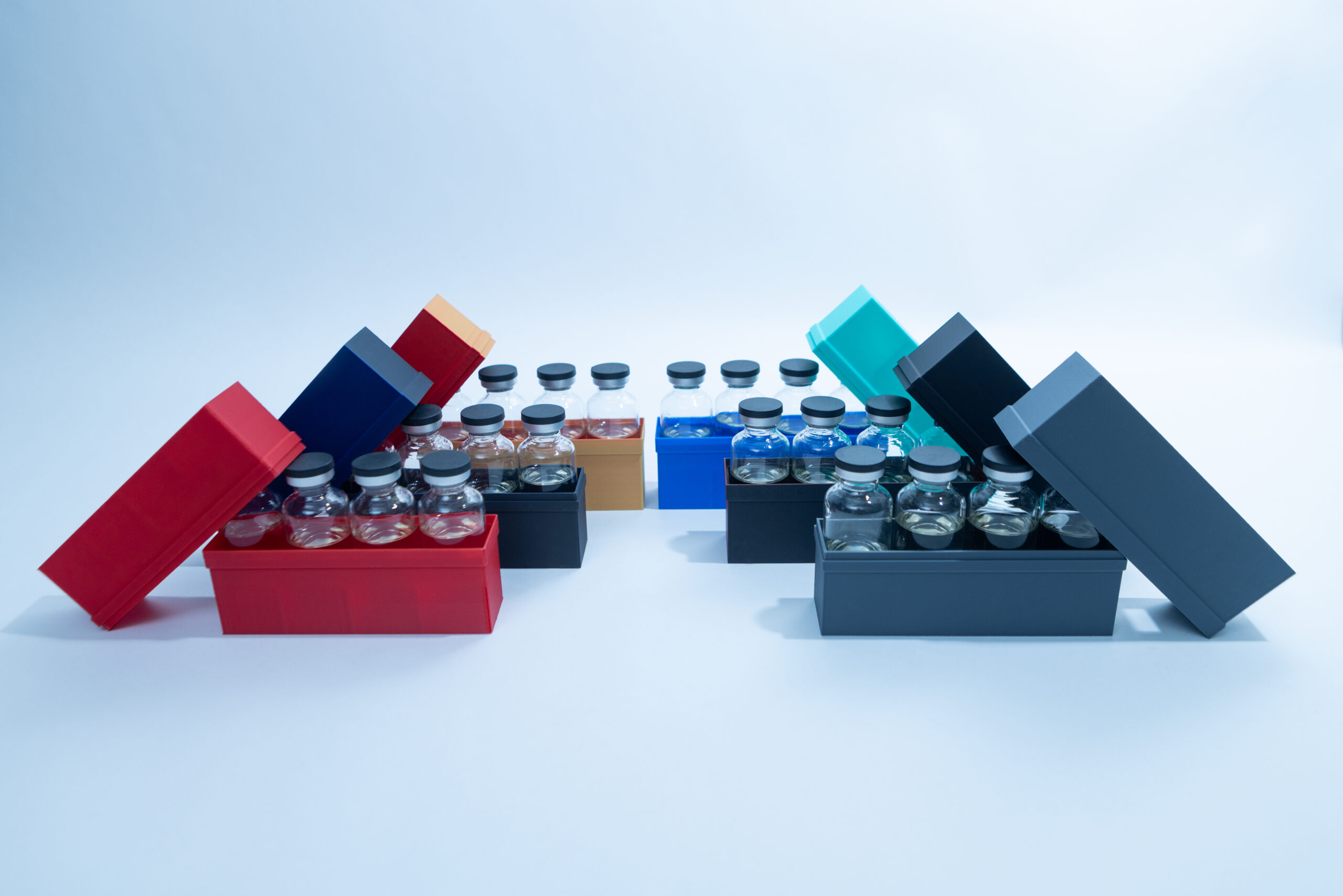 Colorful boxes with lids, each holding glass vials, arranged in two rows against a white background.