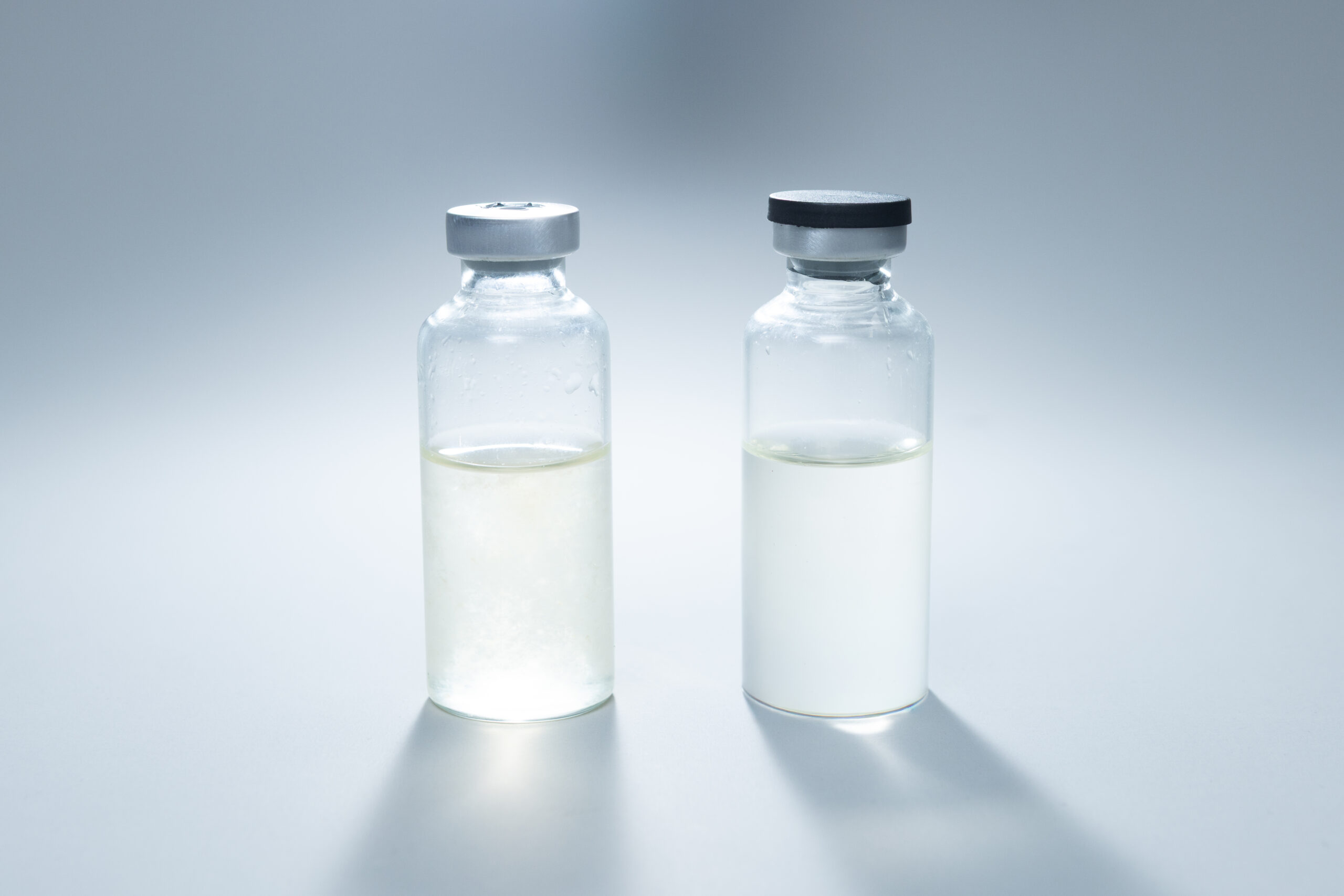 Two clear vials with different colored liquids, one yellowish and one milky white, on a light surface.
