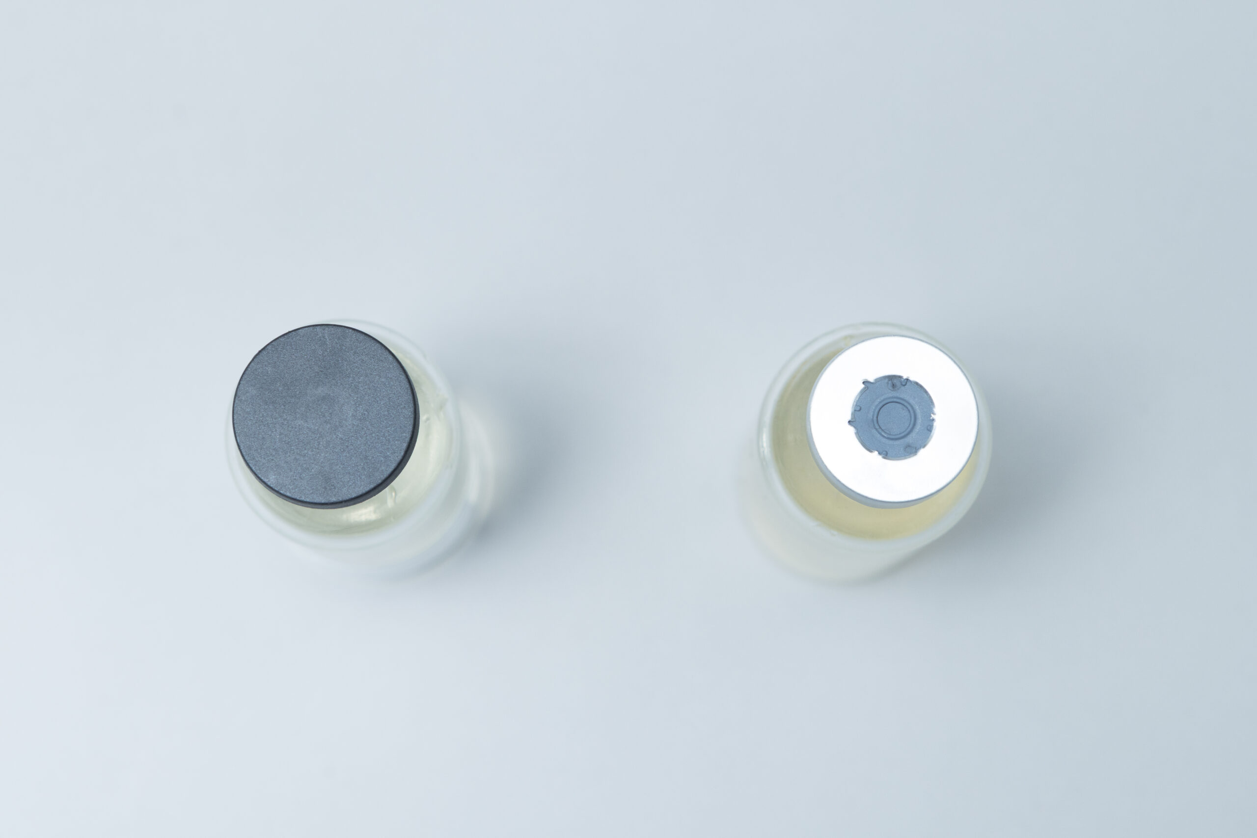 Two glass vials with silver and gray caps are placed side by side on a white background.