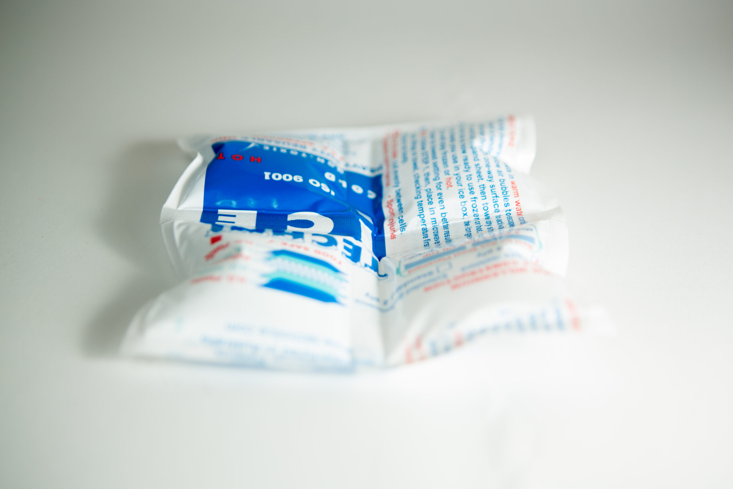 A white instant ice pack with blue and red text lies on a white surface.