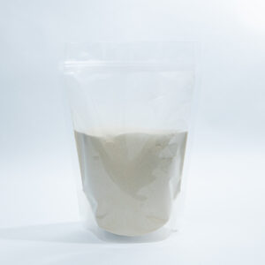 A clear plastic pouch filled with light beige powder stands upright on a white background.