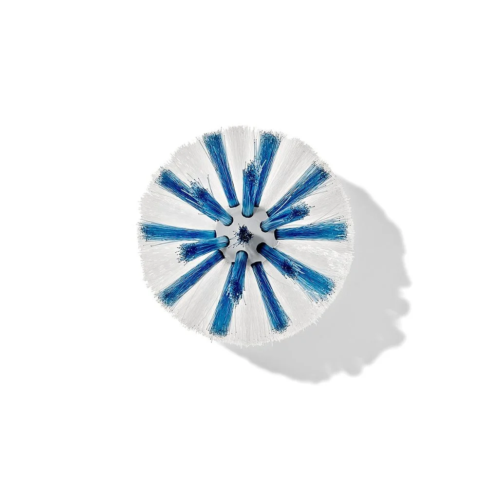 Round scrub brush with white and blue bristles, viewed from above, casting a shadow on a white background.