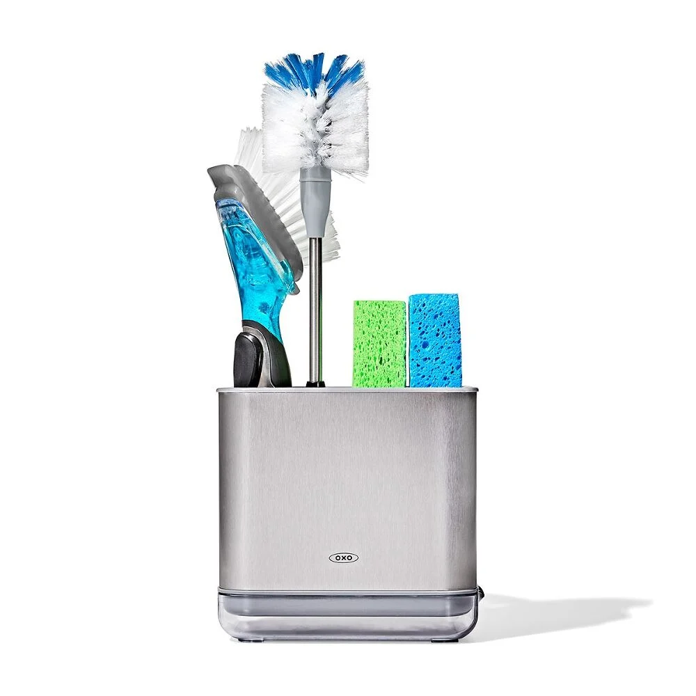 A stainless steel caddy holding two sponges, a dish brush, a bottle brush, and a scrubber.