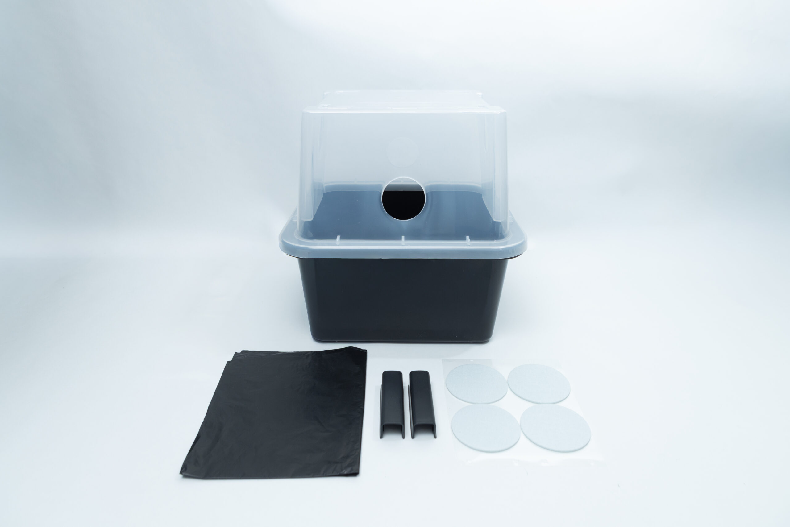 A black and translucent plastic still air box with black plastic sheets, two clips, and four circular filters.